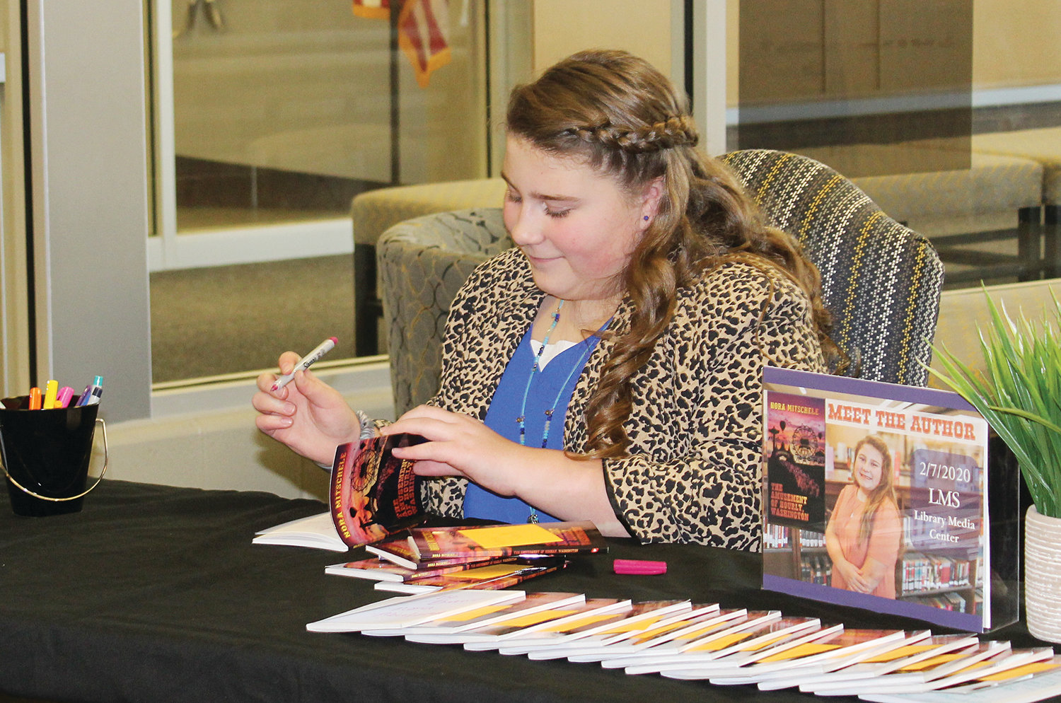 Lebanon Middle School student Nora Mitschele signs copies of her book at a school event Friday.